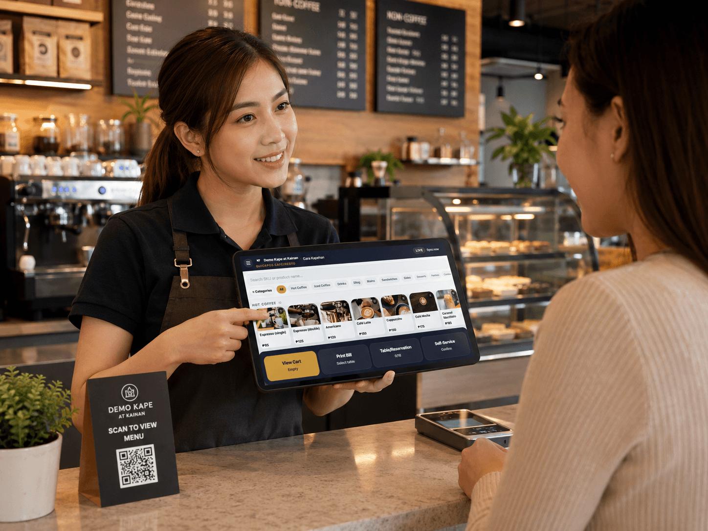 Barista at the counter holding the QuickPOS tablet, taking an order face-to-face with a customer