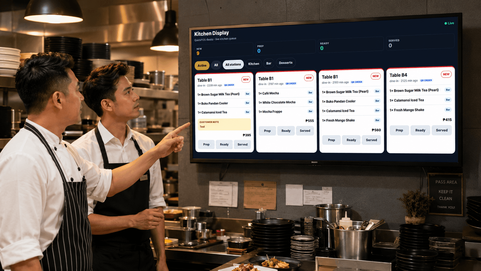 Two cooks at a station looking up at a wall-mounted kitchen display screen showing live orders by table